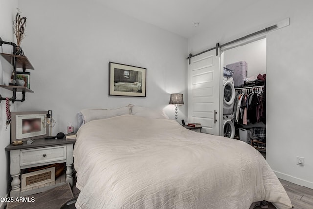 bedroom with a barn door, wood-type flooring, stacked washing maching and dryer, and a closet