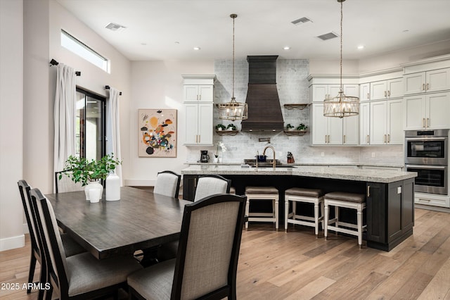 kitchen featuring stainless steel double oven, decorative backsplash, a chandelier, a center island with sink, and recessed lighting