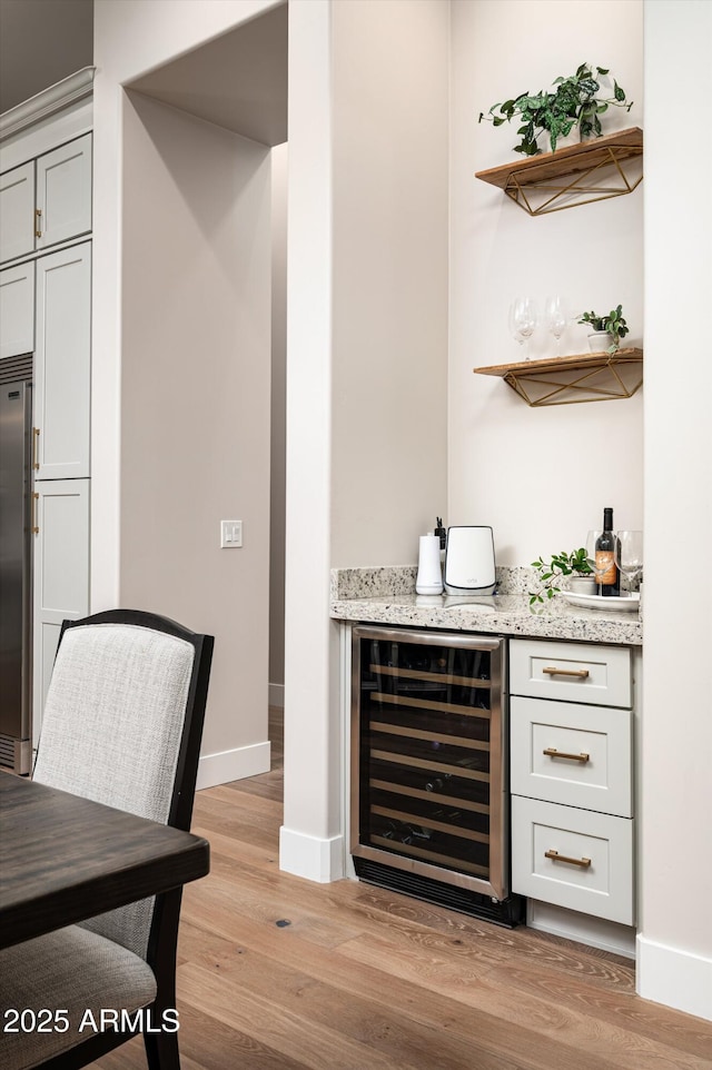 indoor dry bar featuring beverage cooler, light wood-style flooring, baseboards, and stainless steel fridge