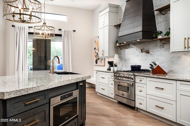 kitchen featuring high end stainless steel range, a sink, a chandelier, custom exhaust hood, and open shelves