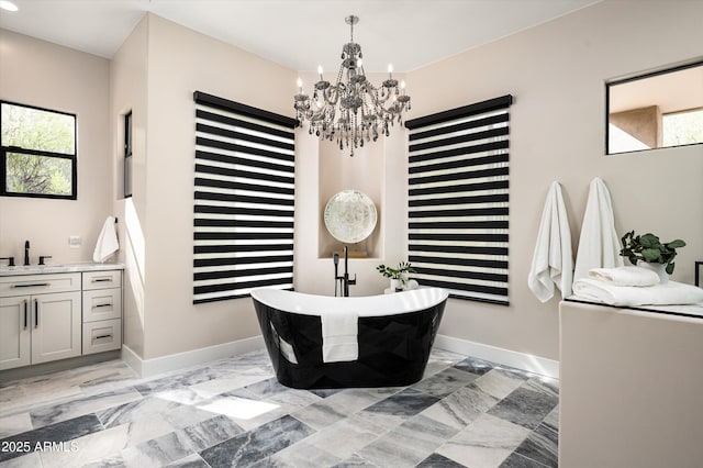 full bathroom with a chandelier, marble finish flooring, a freestanding tub, and baseboards