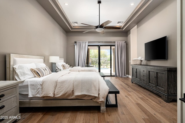 bedroom featuring a tray ceiling, access to exterior, light wood-style flooring, recessed lighting, and a ceiling fan