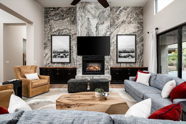 living area featuring wood finished floors, a ceiling fan, a fireplace, and a high ceiling