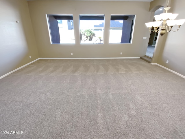 carpeted empty room featuring an inviting chandelier