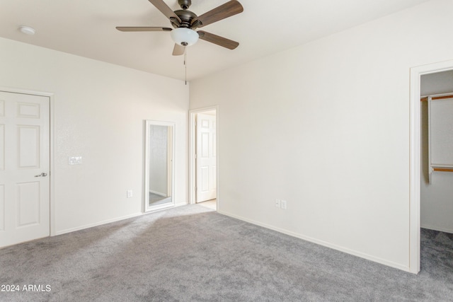 unfurnished bedroom featuring a walk in closet, baseboards, carpet floors, and ceiling fan