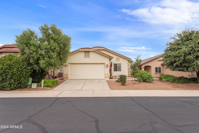 view of front of property with a tile roof, concrete driveway, stucco siding, central AC unit, and an attached garage