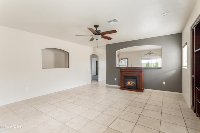 unfurnished living room featuring visible vents, a ceiling fan, a glass covered fireplace, arched walkways, and light tile patterned floors