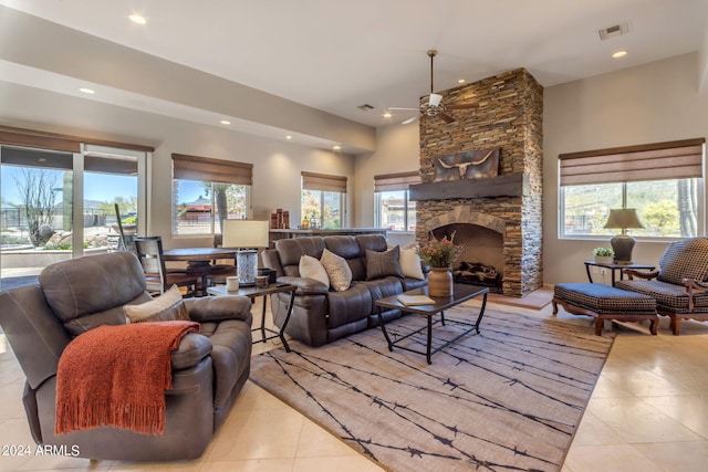 living room featuring ceiling fan, a stone fireplace, and light tile floors