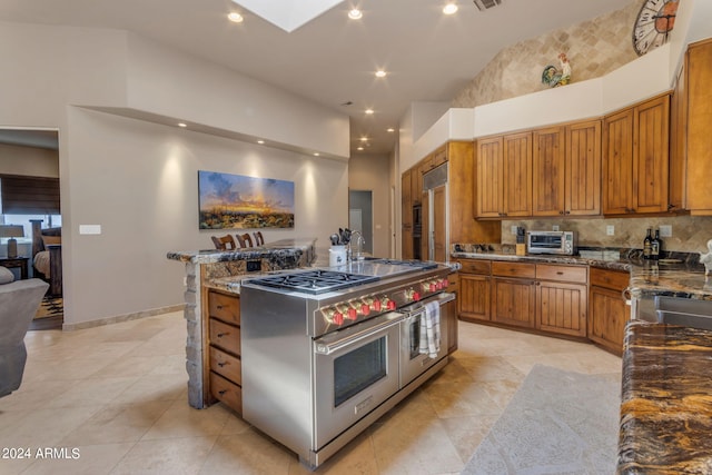 kitchen with range with two ovens, dark stone countertops, high vaulted ceiling, and light tile floors