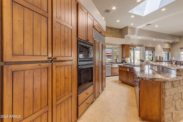 kitchen with black appliances, light tile floors, a skylight, dark stone counters, and a kitchen island