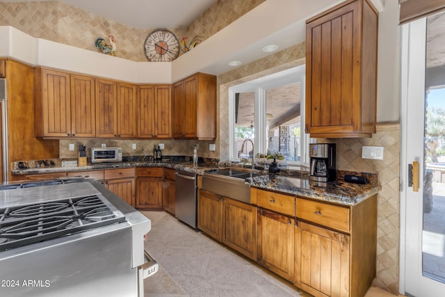 kitchen featuring sink, light tile flooring, backsplash, stainless steel dishwasher, and dark stone countertops