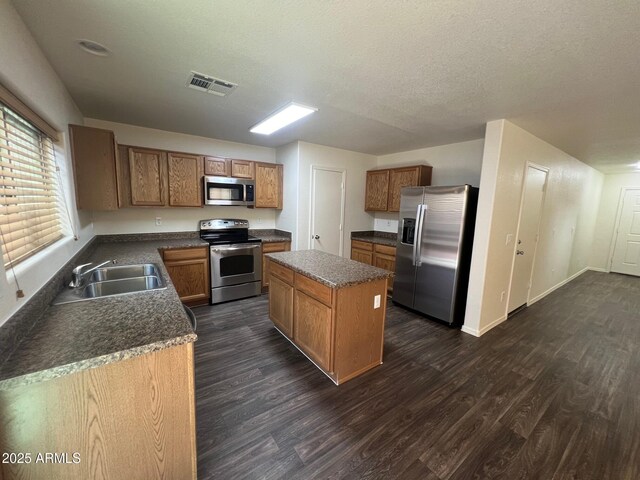 kitchen featuring appliances with stainless steel finishes, a sink, dark wood-type flooring, a center island, and a textured ceiling