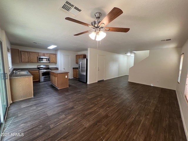 kitchen featuring appliances with stainless steel finishes, open floor plan, a sink, dark wood-style flooring, and a center island