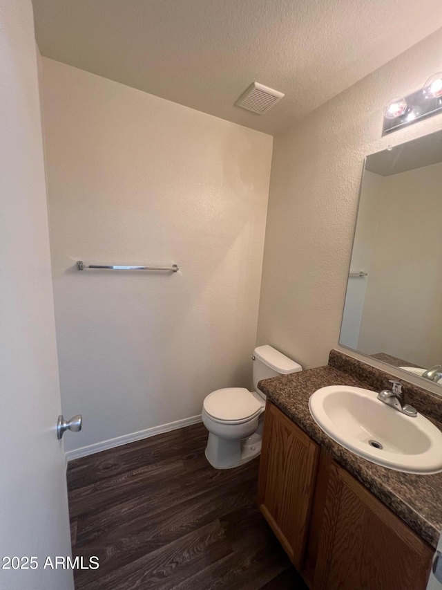 half bathroom with wood finished floors, toilet, vanity, and a textured ceiling