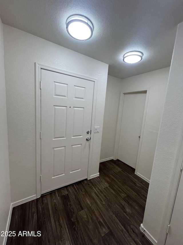 doorway with dark wood-style flooring, a textured ceiling, and baseboards