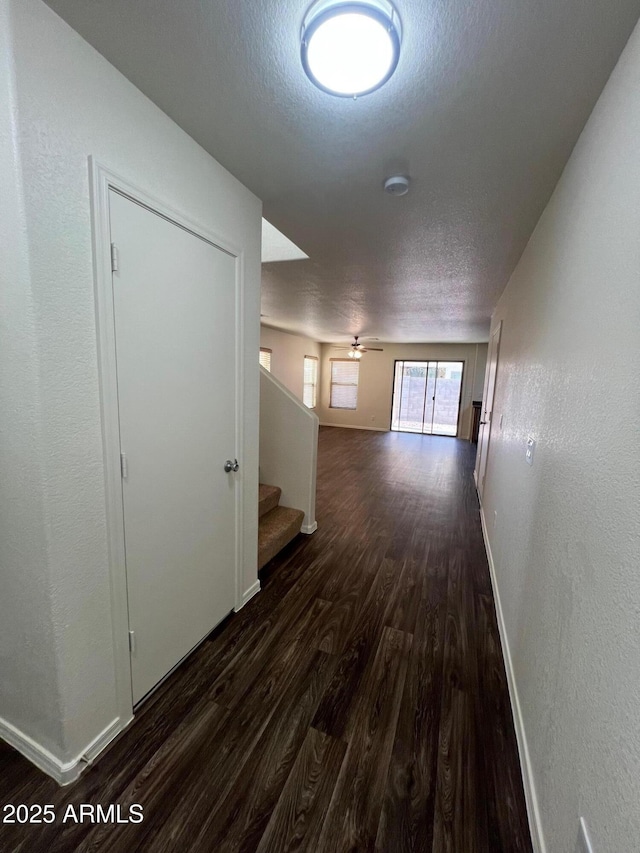 hallway featuring dark wood finished floors, a textured ceiling, stairway, baseboards, and a textured wall