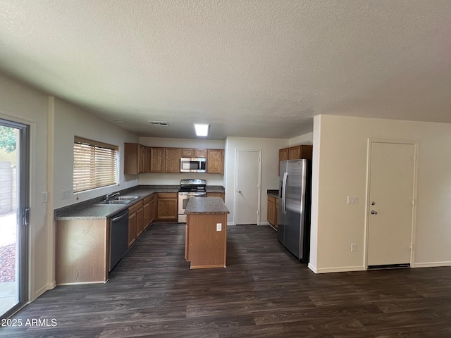 kitchen with appliances with stainless steel finishes, dark countertops, dark wood-type flooring, a textured ceiling, and a center island