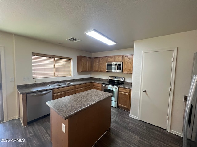 kitchen featuring appliances with stainless steel finishes, a sink, dark wood-type flooring, dark countertops, and a textured ceiling