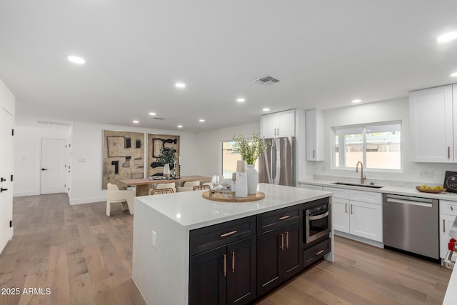 kitchen with appliances with stainless steel finishes, a center island, white cabinets, light hardwood / wood-style flooring, and sink