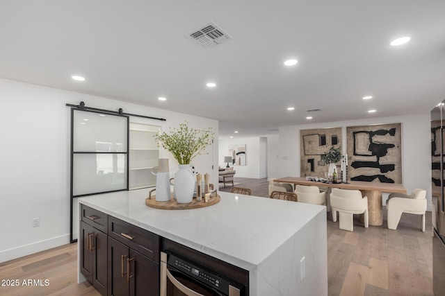 kitchen with a center island, light wood-type flooring, a barn door, and light stone countertops