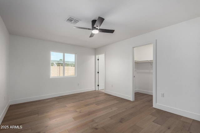 unfurnished bedroom featuring ceiling fan, a walk in closet, hardwood / wood-style floors, and a closet