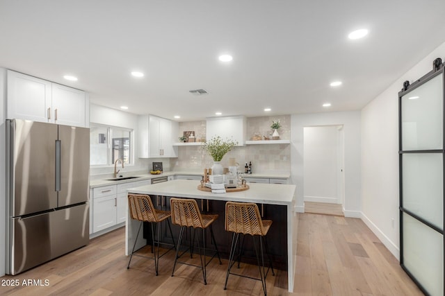 kitchen with sink, white cabinets, stainless steel fridge, and a barn door