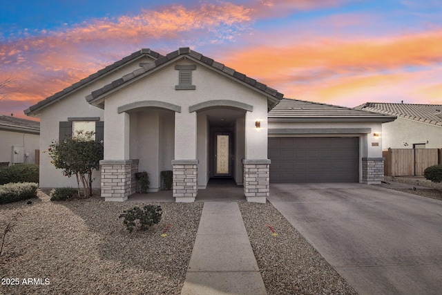 view of front of home with a garage, concrete driveway, stone siding, a tile roof, and stucco siding