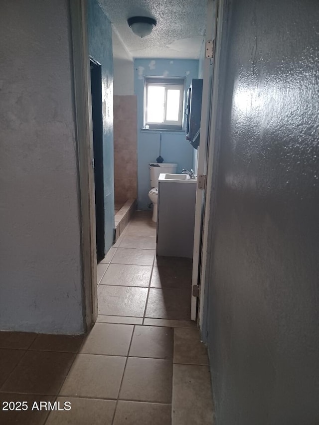 hallway featuring a sink, a textured ceiling, and light tile patterned flooring