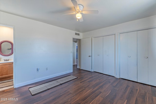 unfurnished bedroom featuring visible vents, baseboards, two closets, and wood finished floors