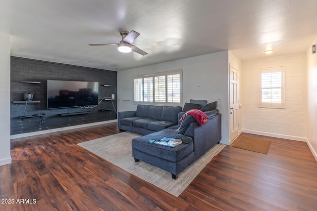 living area with wood finished floors, baseboards, brick wall, and ceiling fan