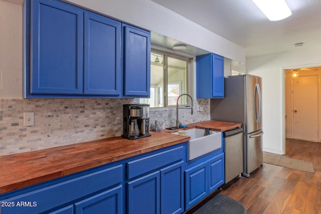 kitchen with butcher block countertops, blue cabinetry, appliances with stainless steel finishes, and a sink