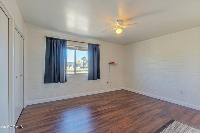 unfurnished room featuring dark wood finished floors, baseboards, brick wall, and ceiling fan