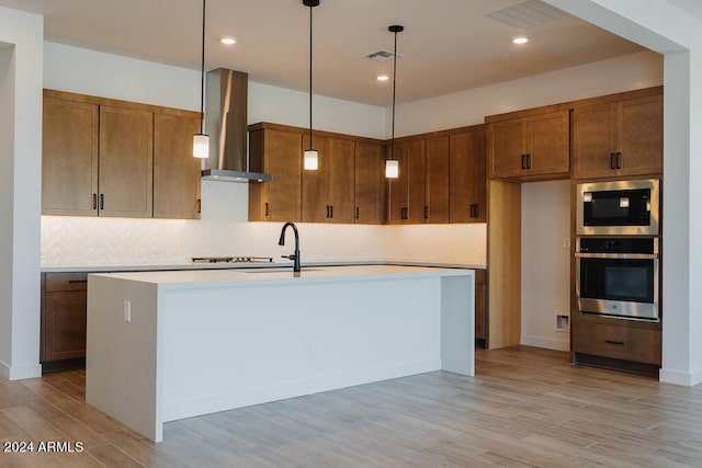 kitchen featuring appliances with stainless steel finishes, wall chimney exhaust hood, decorative light fixtures, and light hardwood / wood-style flooring