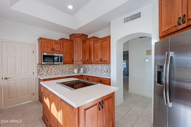 kitchen with a raised ceiling, a kitchen island, appliances with stainless steel finishes, and tasteful backsplash