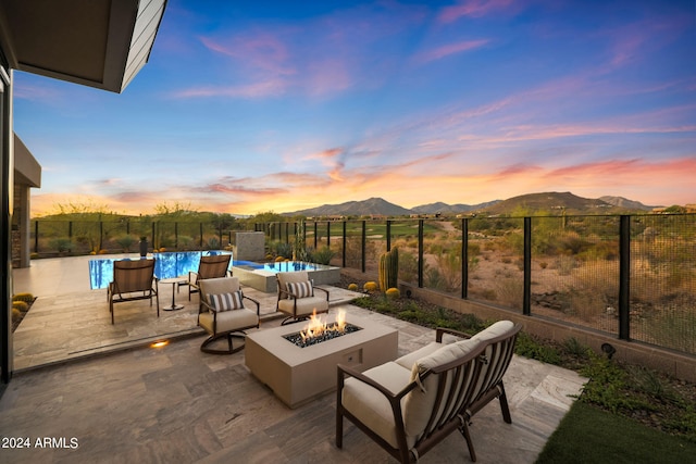 patio terrace at dusk with a mountain view, a fenced in pool, and an outdoor fire pit