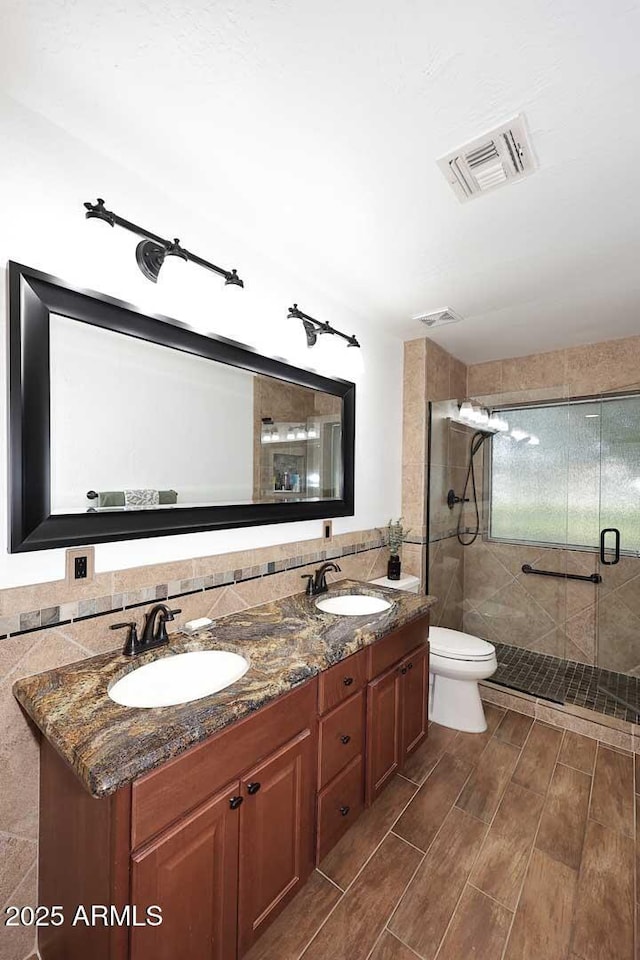 full bath with visible vents, a sink, a stall shower, and double vanity