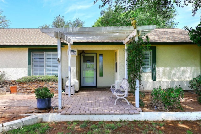 doorway to property featuring a pergola, a patio, roof with shingles, and stucco siding