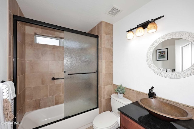 bathroom featuring visible vents, vanity, toilet, tile walls, and enclosed tub / shower combo