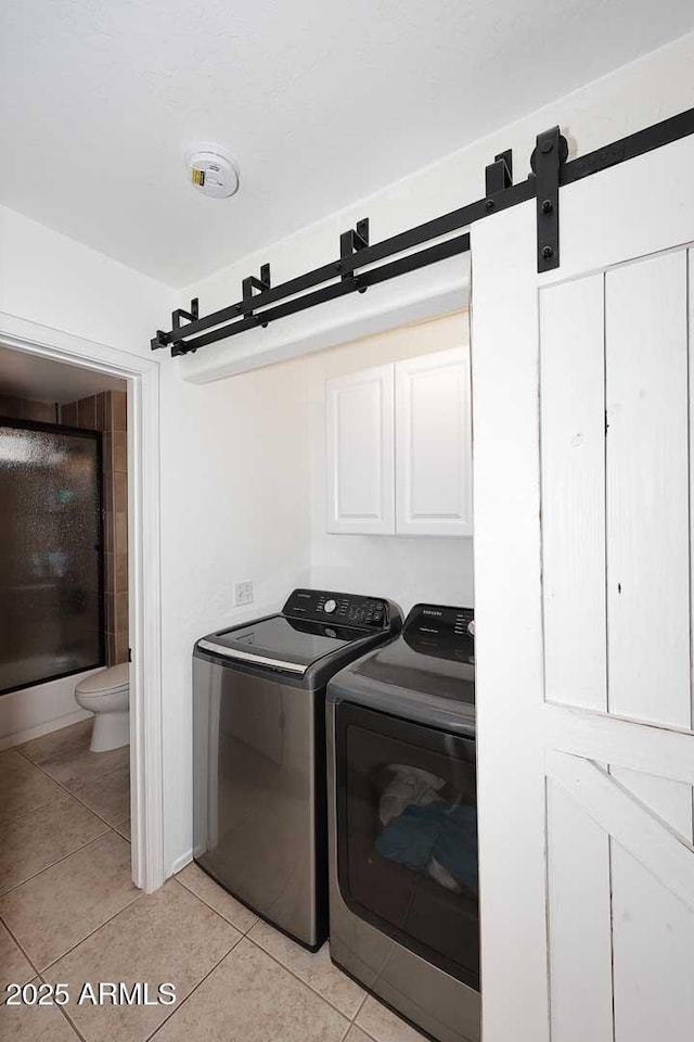 washroom with light tile patterned floors, separate washer and dryer, laundry area, and a barn door