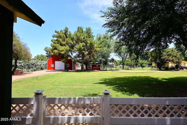 view of yard with fence, a detached garage, an outbuilding, and driveway