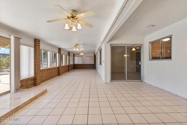 interior space featuring light tile patterned flooring, brick wall, ceiling fan, and a textured ceiling