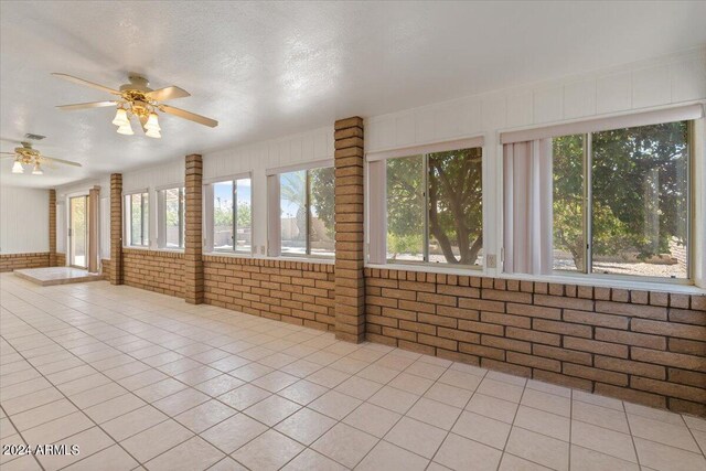 tiled spare room with ceiling fan, plenty of natural light, and brick wall