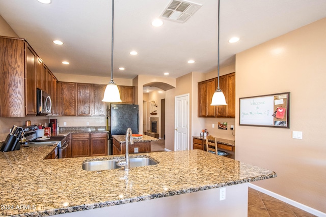 kitchen with kitchen peninsula, light stone counters, stainless steel appliances, sink, and decorative light fixtures