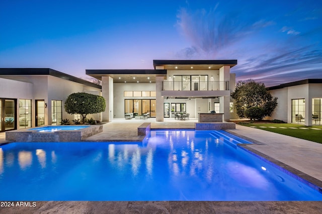 back house at dusk with a pool with hot tub, a patio, and a balcony