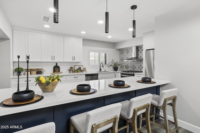 kitchen featuring wall chimney range hood, sink, appliances with stainless steel finishes, white cabinets, and decorative light fixtures