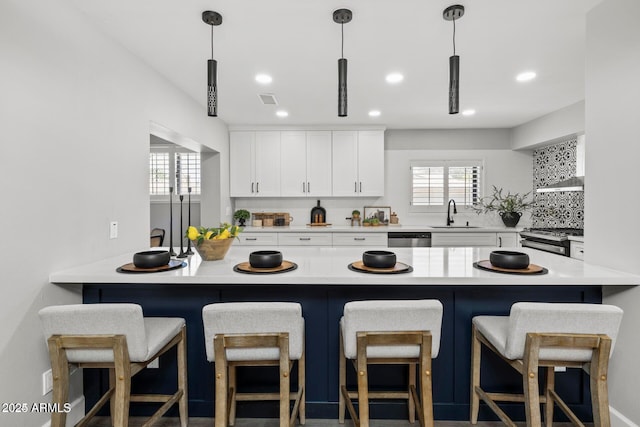 kitchen featuring a breakfast bar area, appliances with stainless steel finishes, white cabinetry, range hood, and decorative light fixtures