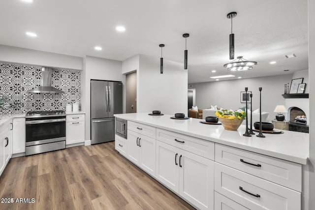 kitchen with pendant lighting, wall chimney range hood, white cabinetry, and stainless steel appliances