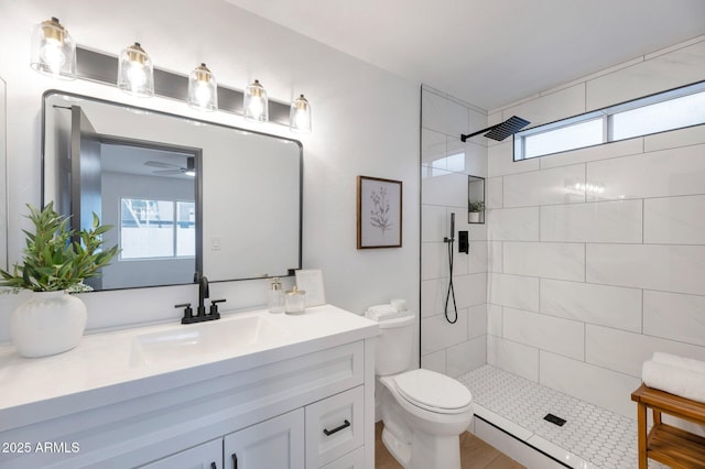 bathroom with vanity, toilet, tiled shower, and a wealth of natural light