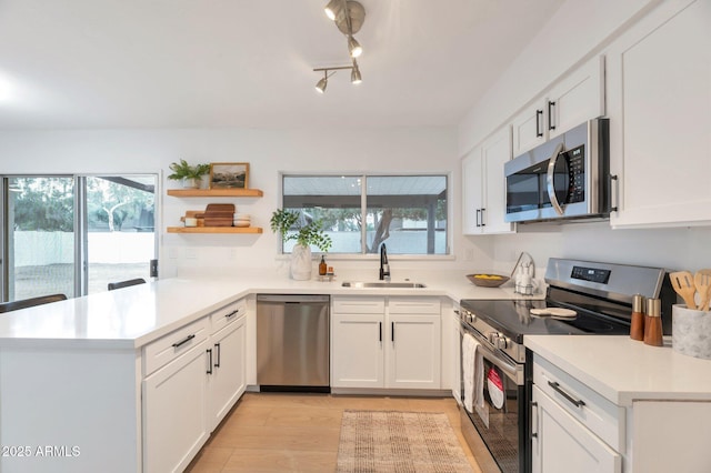 kitchen with white cabinets, kitchen peninsula, sink, and appliances with stainless steel finishes