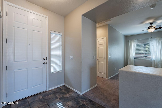 foyer featuring ceiling fan and dark carpet